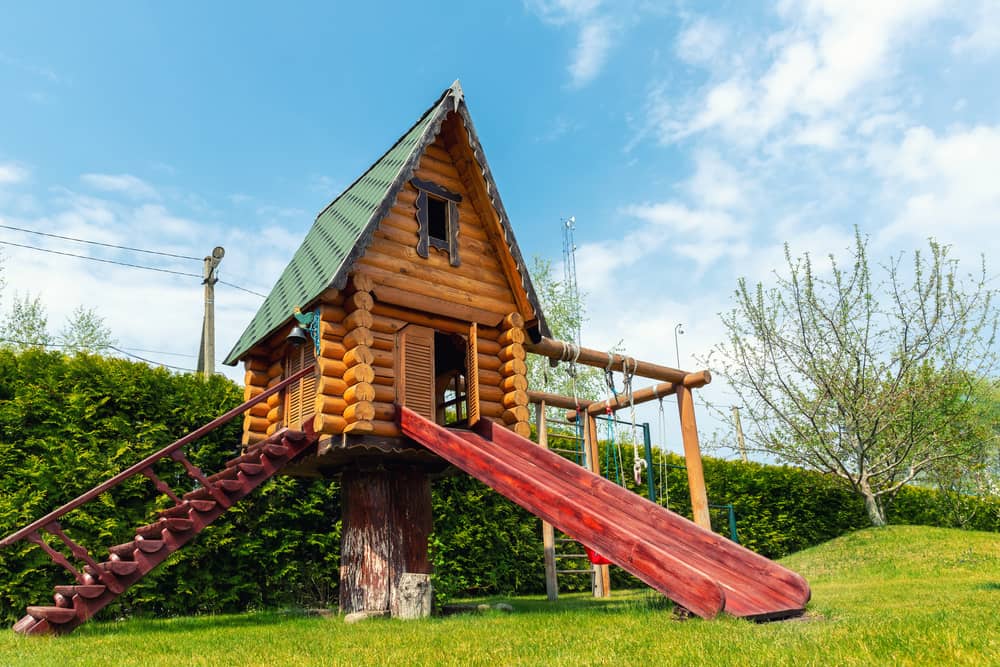 Small wood log playhouse hut with stairs ladder and wooden slide on children playground at park or house yard