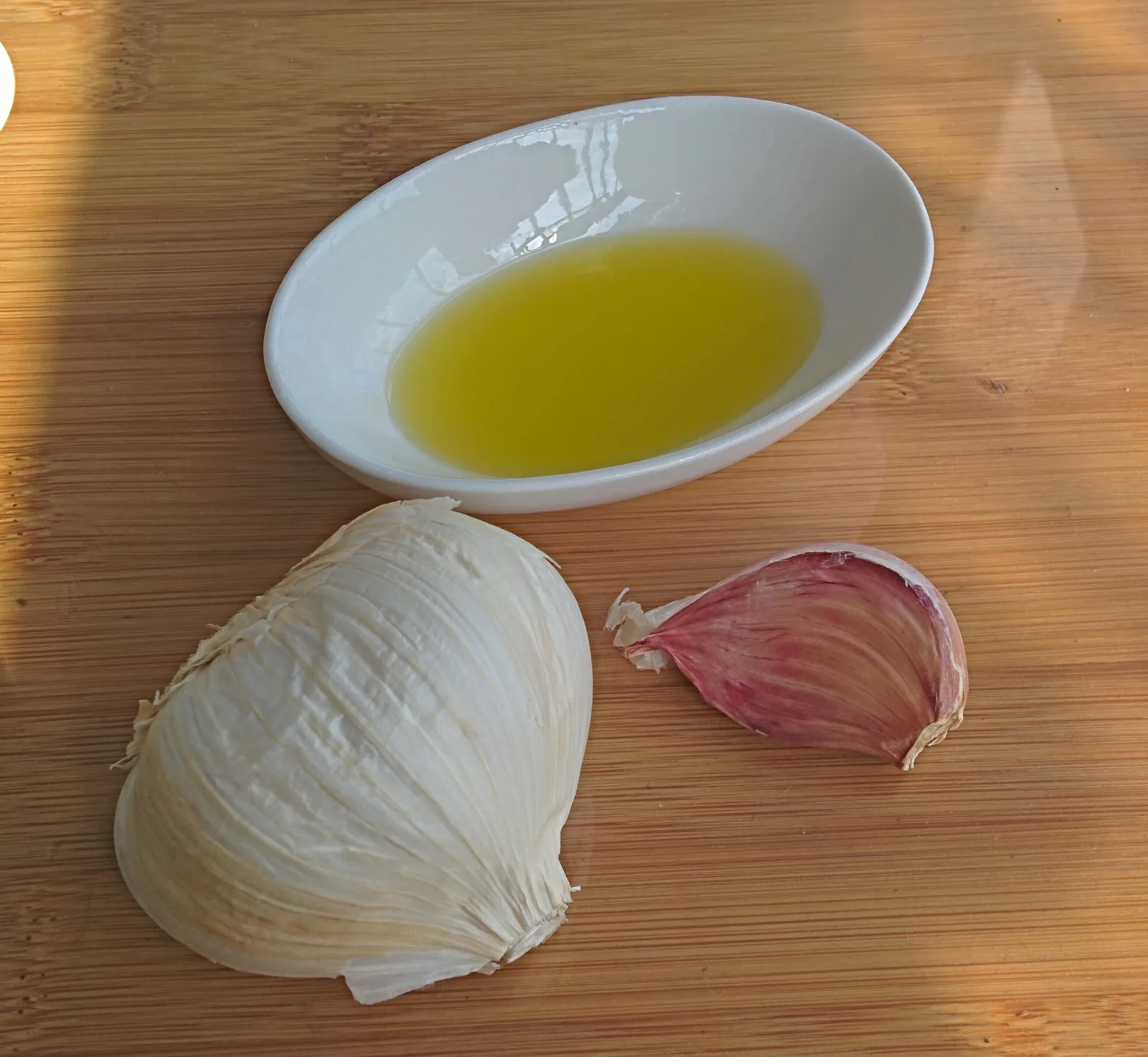 A garlic bulb and clove beside a bowl of oil